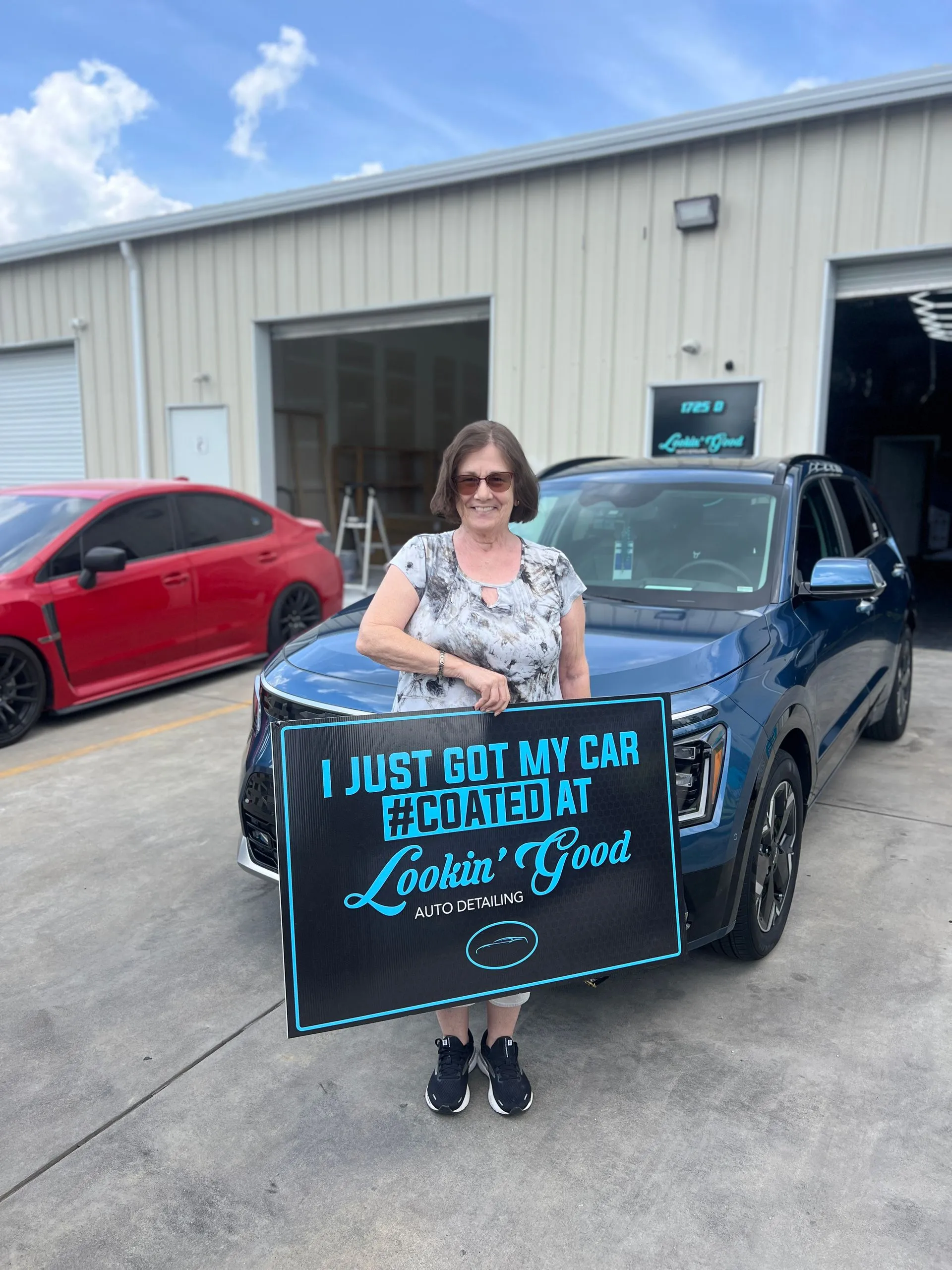 Client holding a #COATED sign beside a coated Kia EV9
