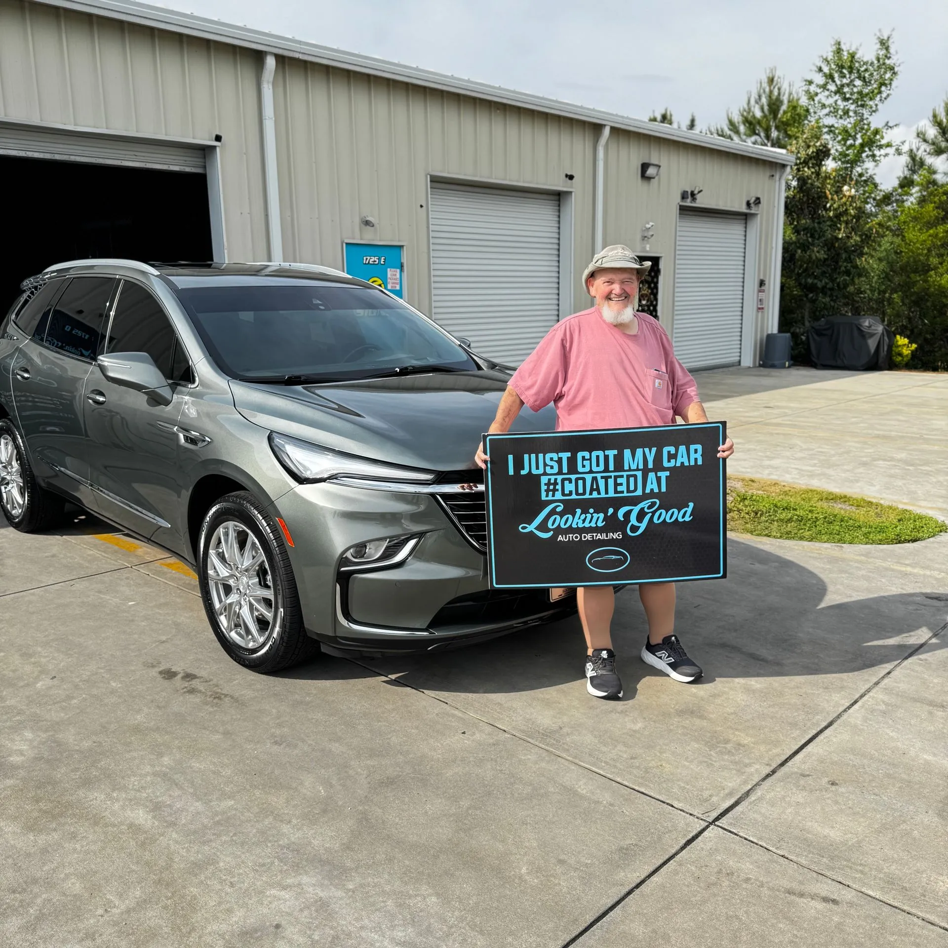 Client holding a #COATED sign beside a coated Buick Enclave at the shop